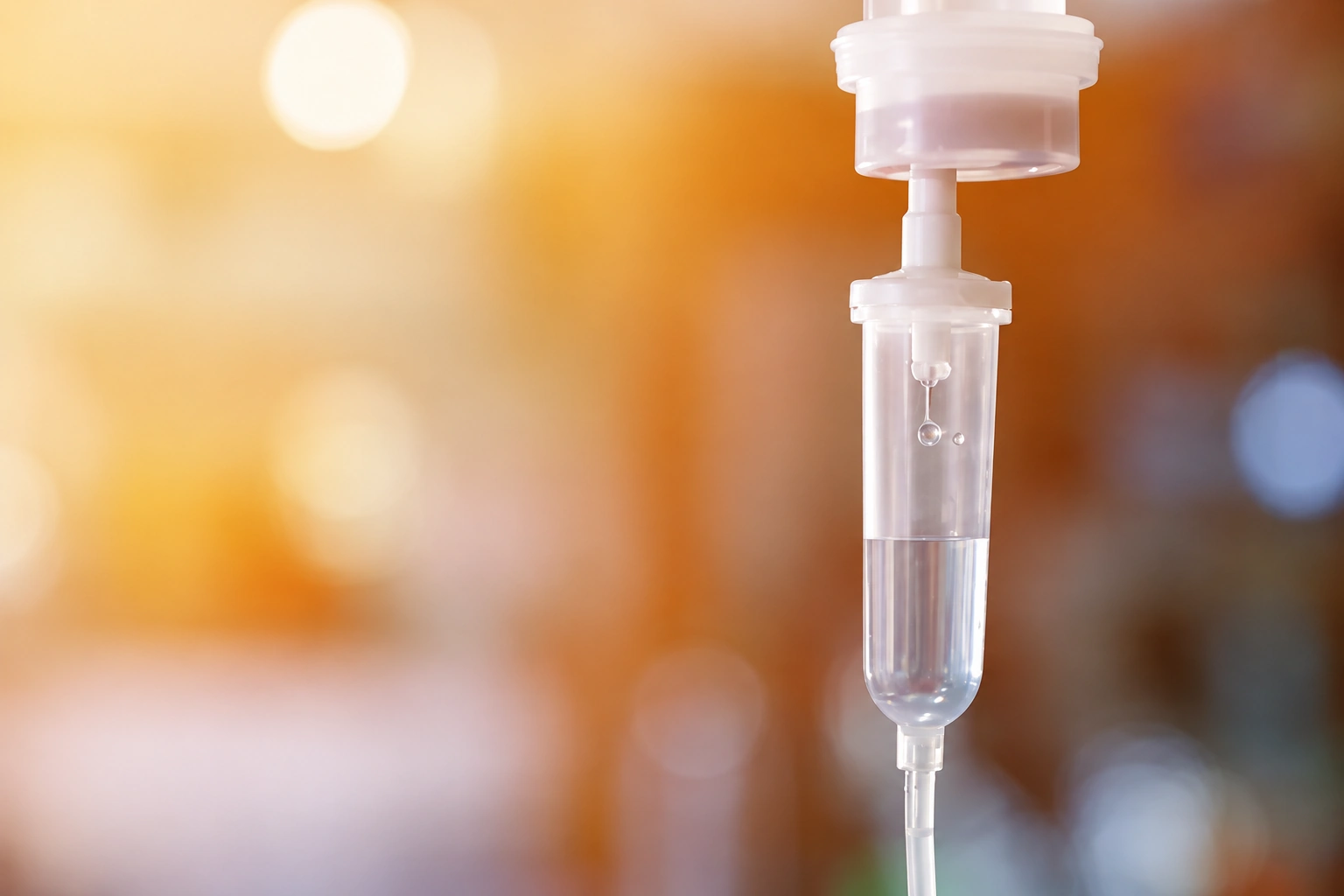 Clear IV drip chamber against a softly lit golden background